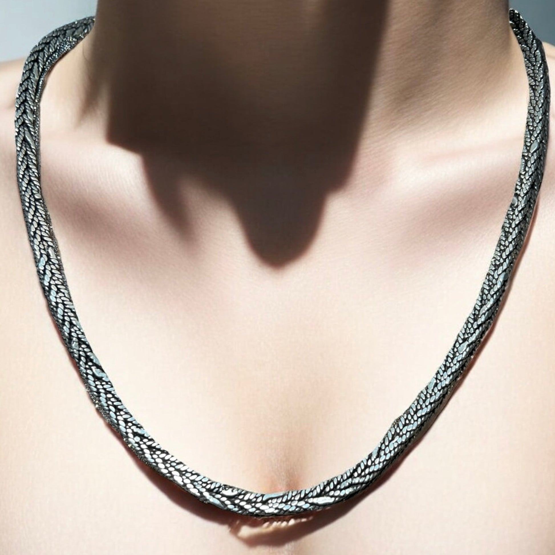 A close-up of a person wearing the Zevaayra Viraat Chain, a textured, handcrafted Indian sterling silver necklace that rests on their bare neck and collarbone with soft shadows on the skin.