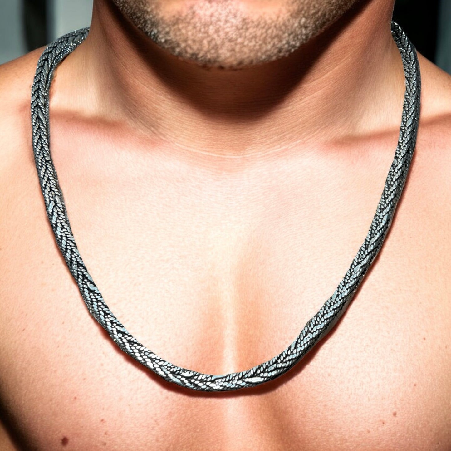 A close-up of a mans chest and neck showcases the Zevaayra Viraat Chain, a thick, textured oxidized sterling silver necklace. The focus is on the unique jewelry, with the man’s face not fully visible.