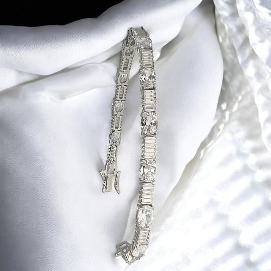 The Zevaayra Victoria Royale Bracelet, featuring oval-cut stones and assorted clear gemstones, is showcased on soft white textured fabric under bright lighting.