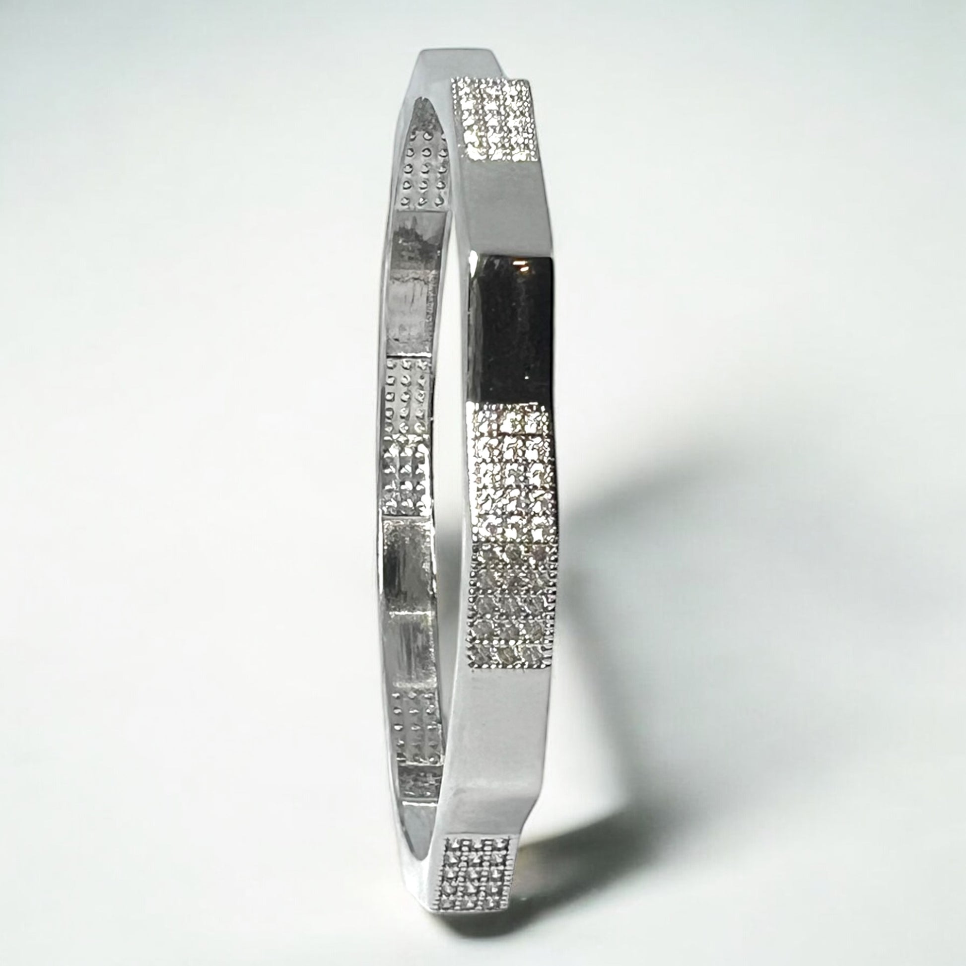 The Zeneer Cuff – Polished Silver Brilliance by Zevaayra is a sterling silver bracelet with alternating smooth and textured sections accented by sparkling cubic zirconia, showcased against a plain white background.