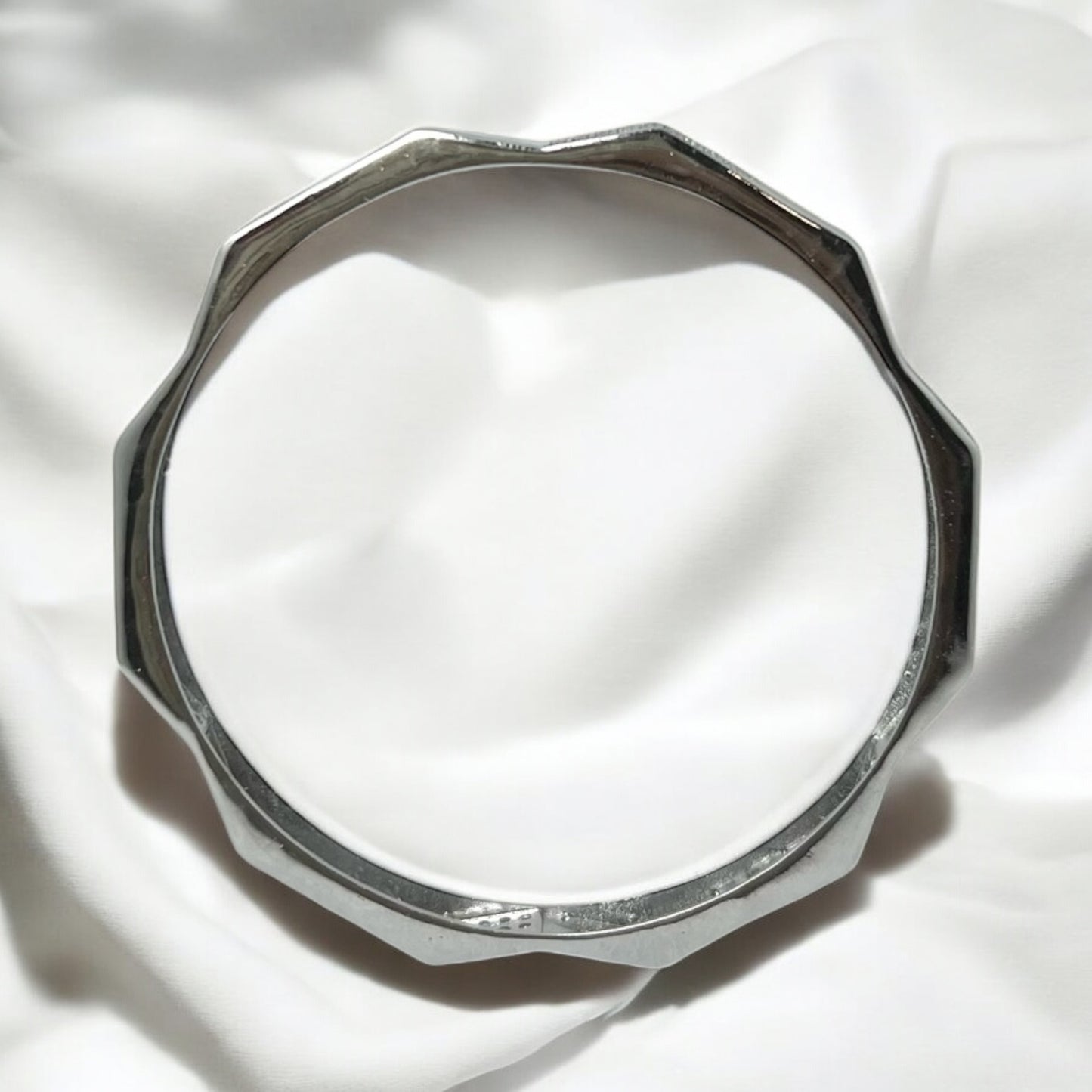 The Zeneer Cuff – Polished Silver Brilliance by Zevaayra features a sleek, faceted design and gleams against soft white fabric—an elegant sterling silver accessory that elevates any look.