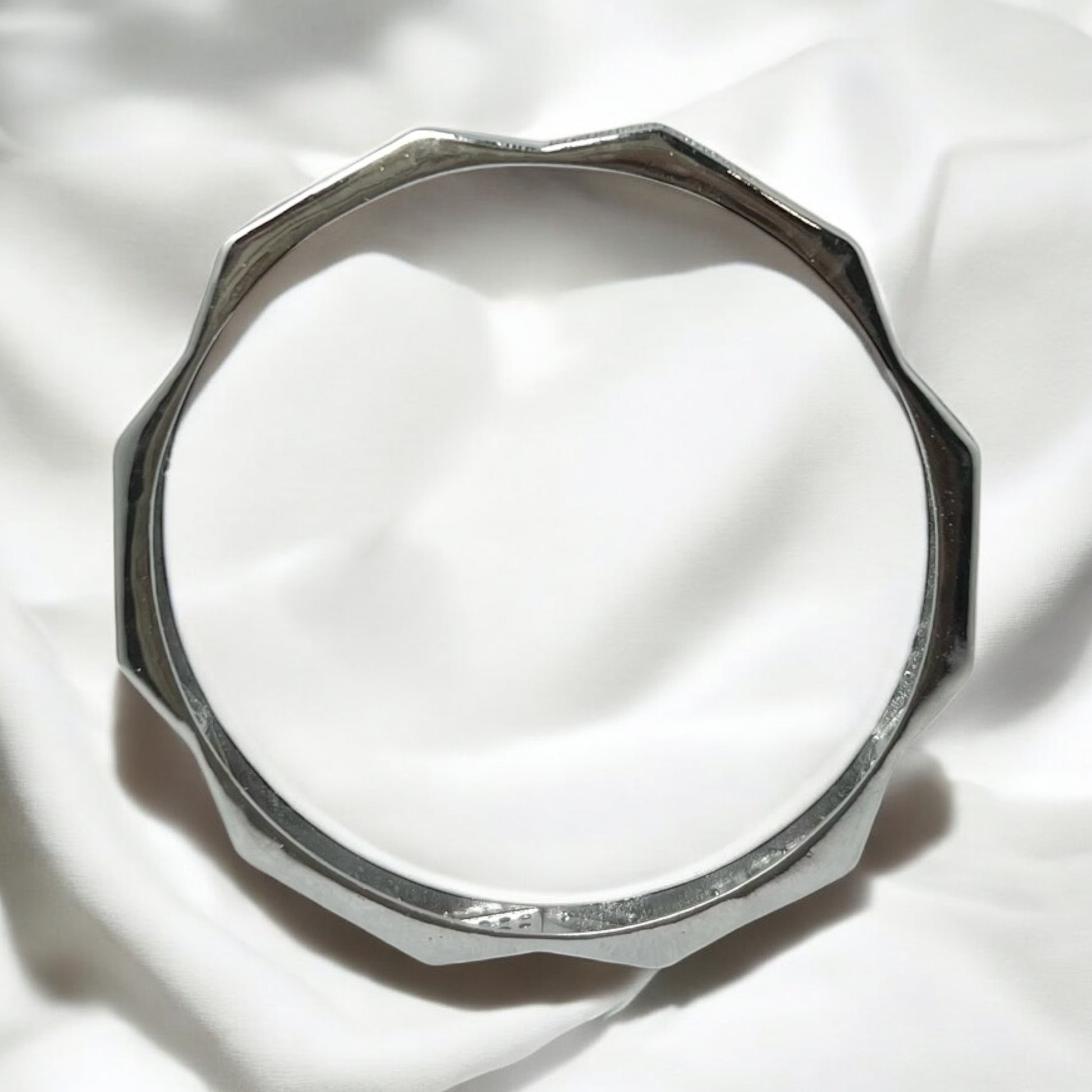 The Zeneer Cuff – Polished Silver Brilliance by Zevaayra features a sleek, faceted design and gleams against soft white fabric—an elegant sterling silver accessory that elevates any look.