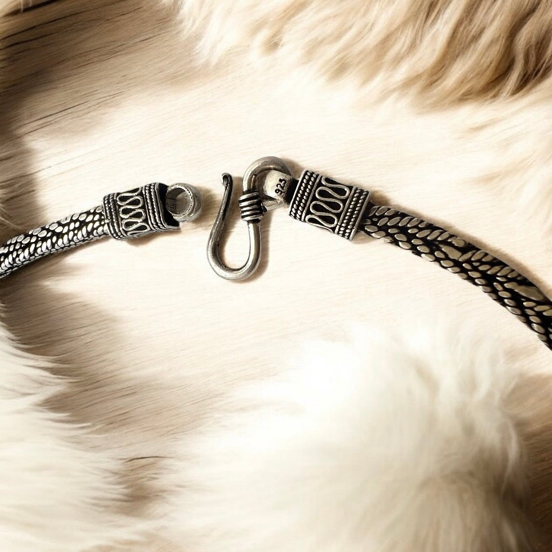 A close-up of the Zevaayra Viraat Chain, a handcrafted Indian necklace with an oxidized silver chain, intricate patterns, and a decorative hook clasp, displayed on a light wooden surface with soft white fur around it.