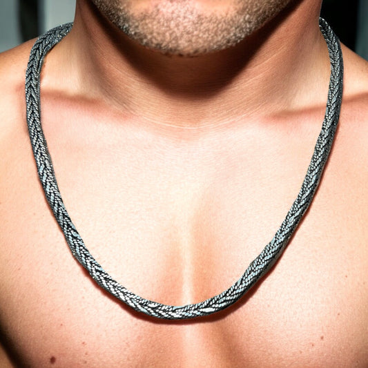 A close-up of a mans chest and neck showcases the Zevaayra Viraat Chain, a thick, textured oxidized sterling silver necklace. The focus is on the unique jewelry, with the man’s face not fully visible.