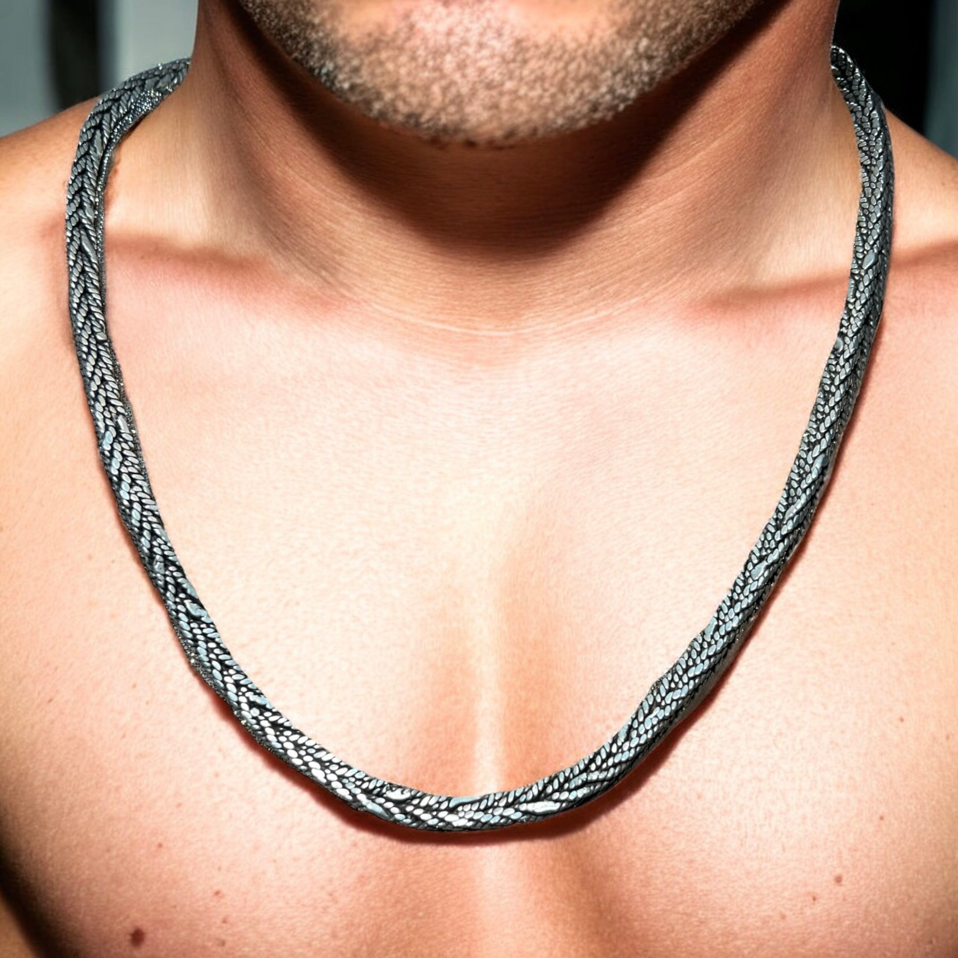 A close-up of a mans chest and neck showcases the Zevaayra Viraat Chain, a thick, textured oxidized sterling silver necklace. The focus is on the unique jewelry, with the man’s face not fully visible.