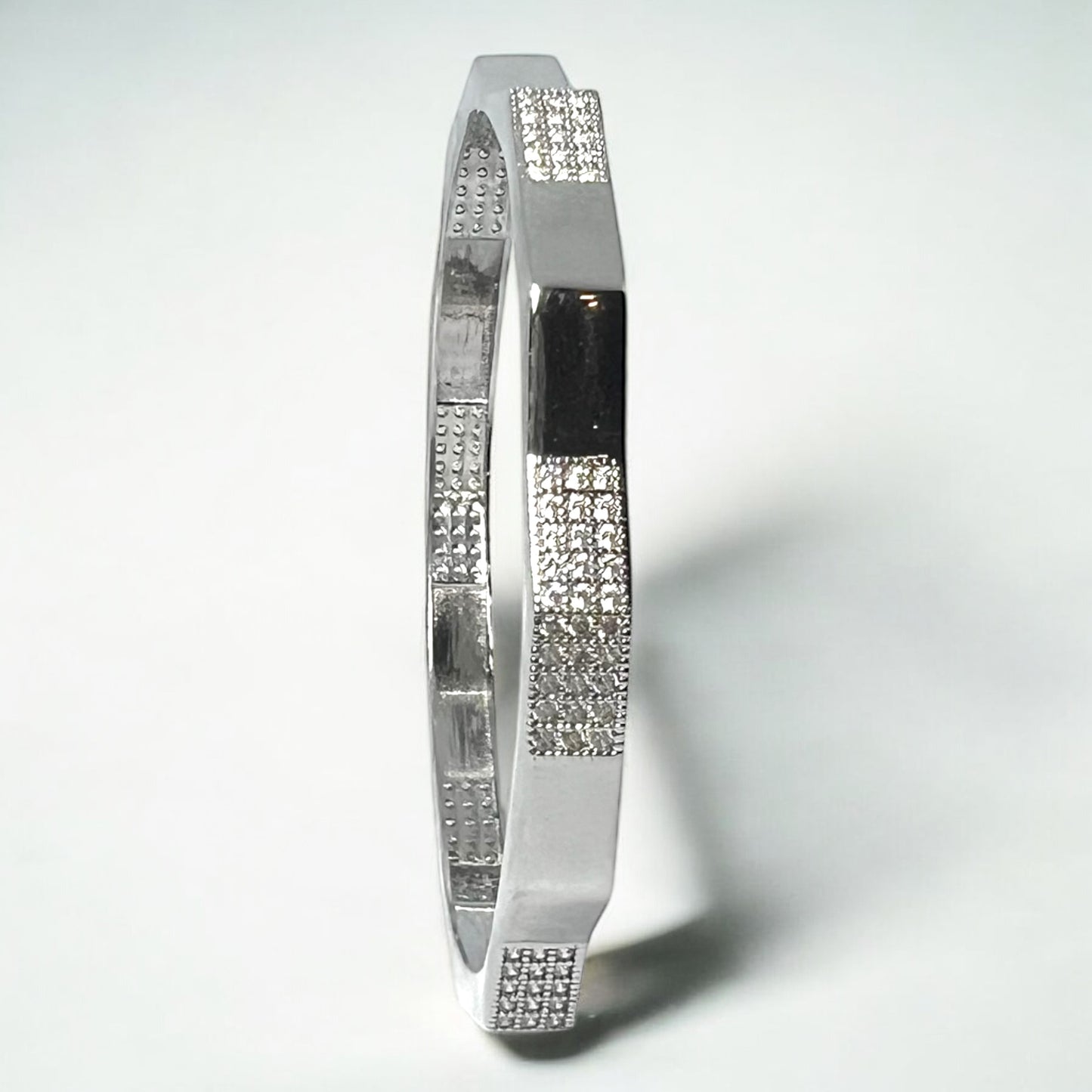 The Zeneer Cuff – Polished Silver Brilliance by Zevaayra is a sterling silver bracelet with alternating smooth and textured sections accented by sparkling cubic zirconia, showcased against a plain white background.