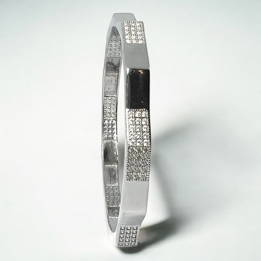 The Zeneer Cuff – Polished Silver Brilliance by Zevaayra is a sterling silver bracelet with alternating smooth and textured sections accented by sparkling cubic zirconia, showcased against a plain white background.
